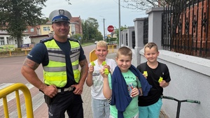 Policjant stoi z trzema uczniami szkoły, uczniowie mają w rękach odblaski, które otrzymały od funkcjonariusza
