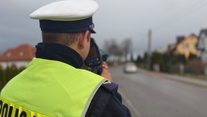Policjant Wydziału Ruchu Drogowego kontrolujący prędkość. W ręku trzyma ręczny miernik prędkości.