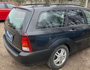 na zdjęciu znajduje się pojazd marki Ford, koloru granatowego, w tle widać fragment pojazdu koloru czerwonego, betonowe ogrodzenie i drzewa.