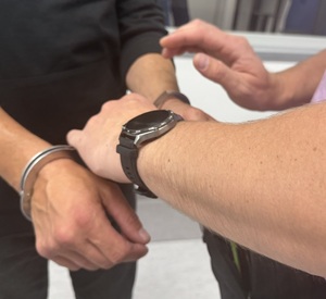 Trzy zdjęcia:
Na pierwszym ręce, z kajdankami, na drugim zdjęciu mężczyzna siedzący w tle, na trzecim ręce, na które policjantka zapina kajdanki